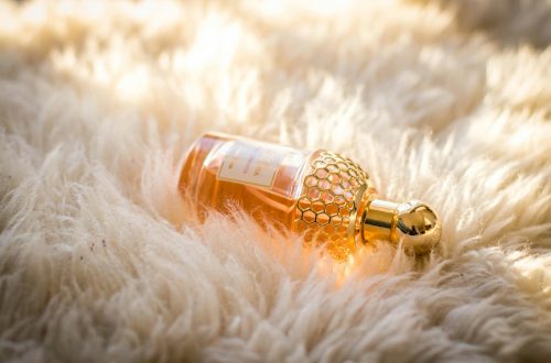 Elegant perfume bottle with gold details resting on fluffy white fur, capturing luxury and glamour.